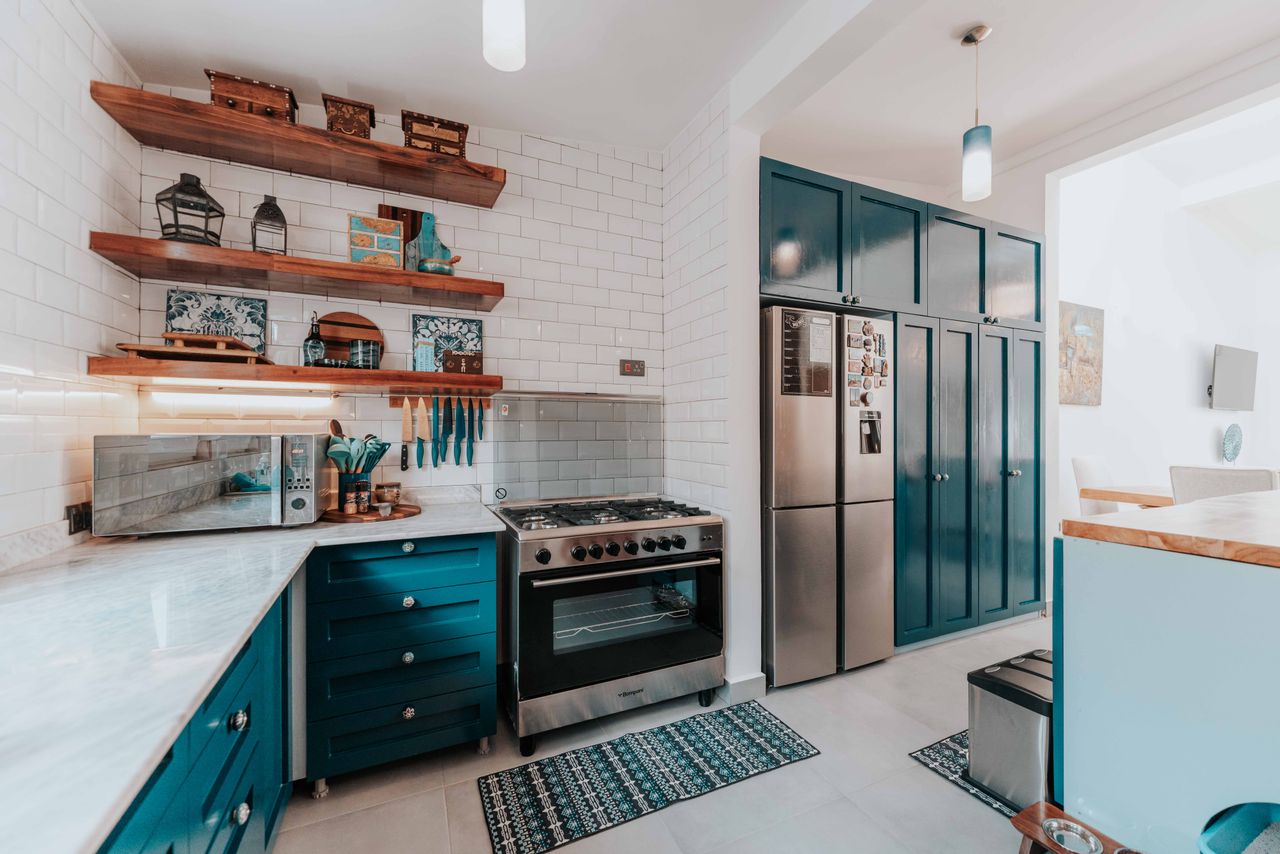 Stylish kitchen featuring sleek blue cabinets, stainless steel appliances, and wooden shelves.
