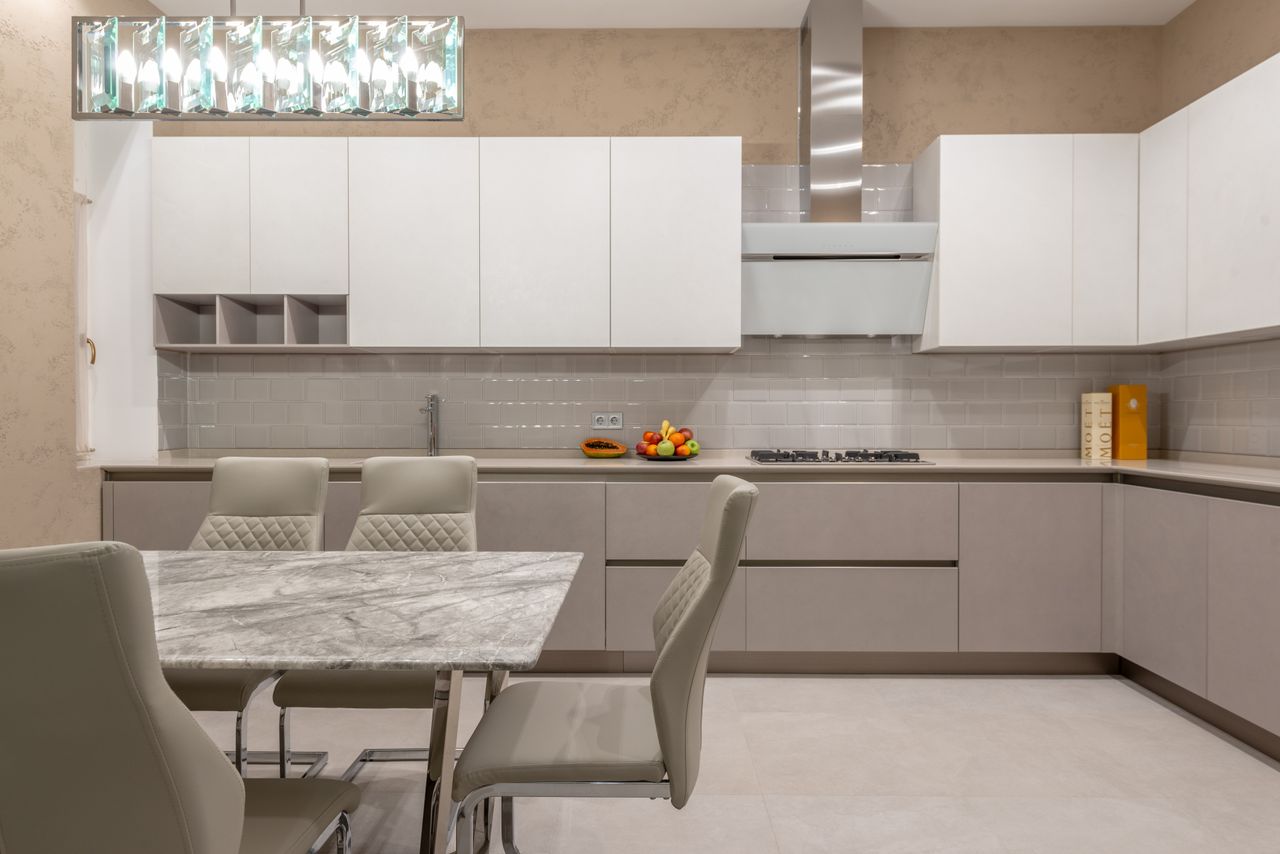 Table with chairs placed near light cupboards and kitchen counter with stove and sink in stylish apartment with modern design